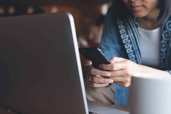 a woman holding a phone before  a laptop