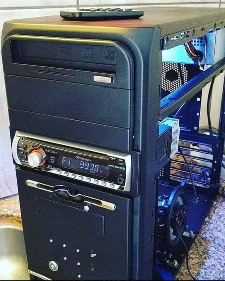 Photo of an open computer chassis that has a DVD drive, an AM/FM/CD car radio, and a 3½ floppy drive installed in front. The remote for the radio can be seen sitting on top of the desktop ready to play the classic rock hits of the 70s, 80s, and 90s. Next up, Imagine Dragons.
