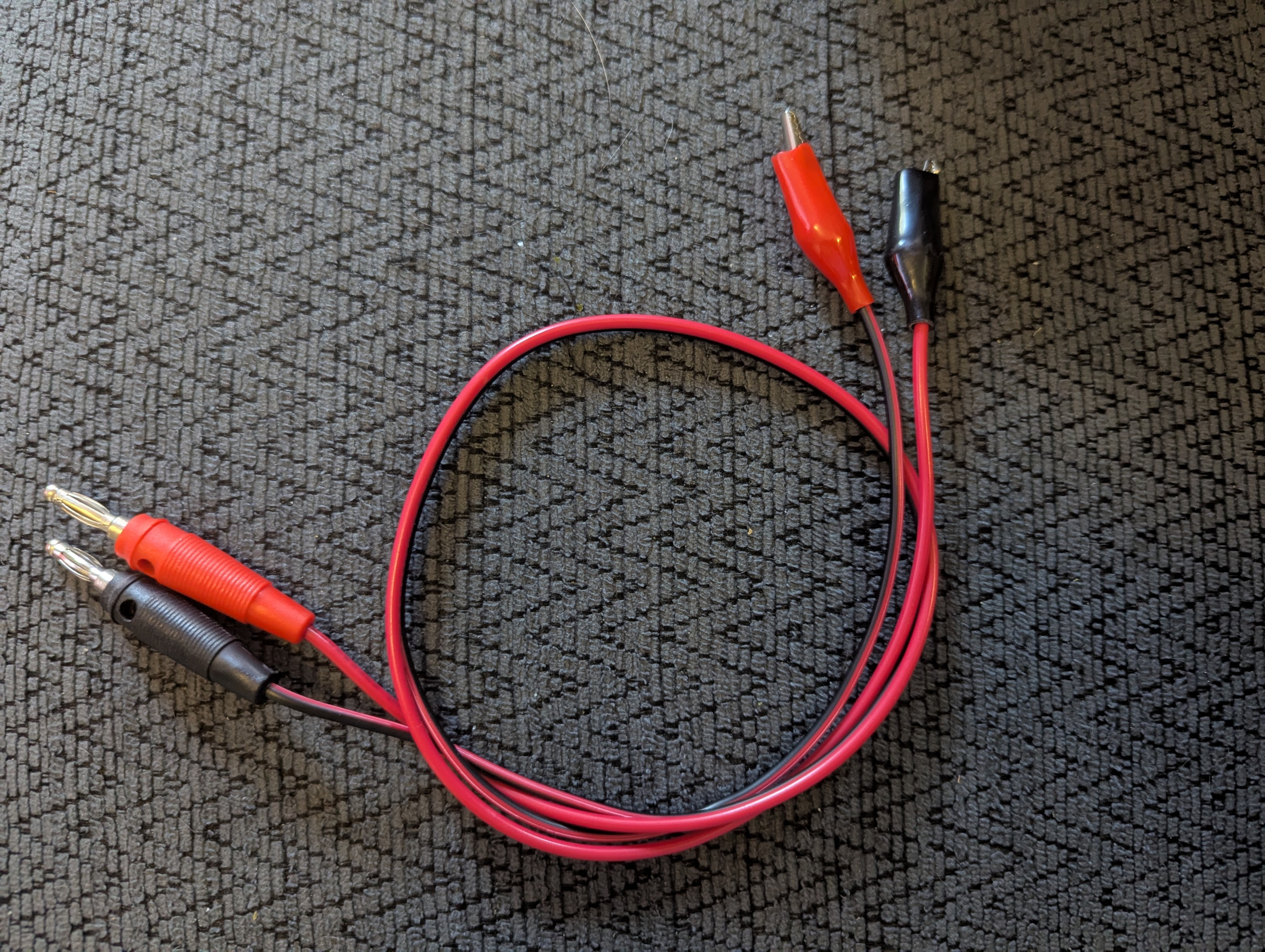 A test cable with alligator clips on one end and banana plugs on the other. There are two wires molded together, one black and one red. The red wire has a red connector on one end and a black connector on the other. The black wire is similarly mixed up except that the wire itself is also half red.