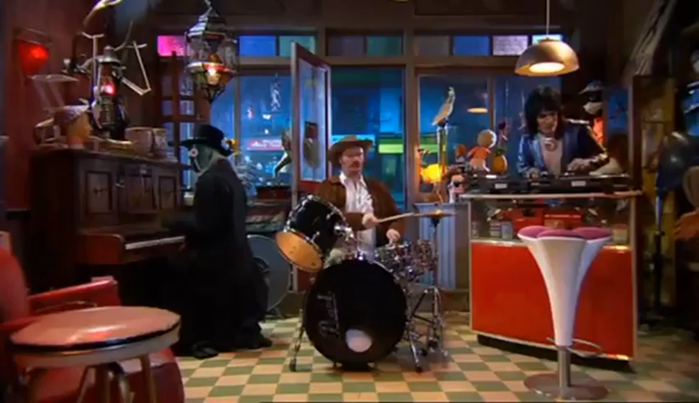 The video showcases a vibrant and eclectic scene set in a lively bar or music venue, characterized by a checkered floor and a warm, inviting atmosphere. The setting is rich with musical instruments, including a piano, drums, and a turntable, along with various decorative items like mannequins and a gramophone, enhancing the whimsical ambiance.

The video begins with a person in a brown jacket and cowboy hat playing the drums, while another individual in a black suit and top hat plays the piano.…