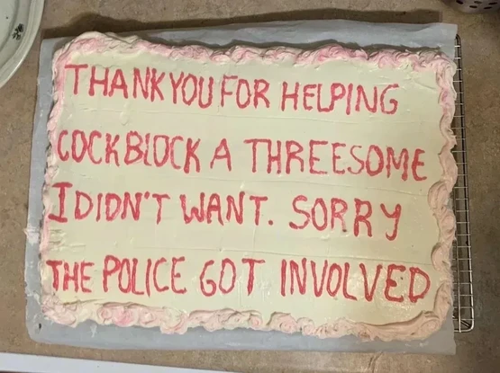 The image shows a rectangular cake with white frosting and red lettering. The cake is sitting on a metal cooling rack, which is placed on a surface that appears to be a countertop. The cake is decorated with pink frosting along the edges in a wavy design. The red lettering on the cake reads, "THANK YOU FOR HELPING COCKBLOCK A THREESOME I DIDN'T WANT. SORRY THE POLICE GOT INVOLVED." The lettering is somewhat uneven, suggesting it was written by hand. The composition is a close-up shot, focusing …