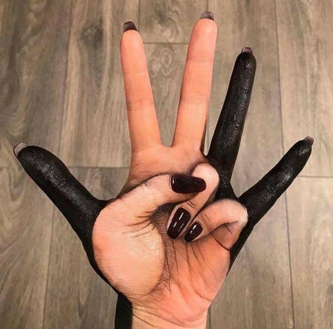 Photo of a hand spread out, palm up, with some body paint on it to make it look like the hand is holding up two fingers, even though it's really just all five spread out.