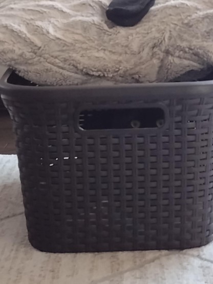 Photo of a laundry basket with two cat eyes from a black cat peaking through the hole on the side. Always watching (or listening)