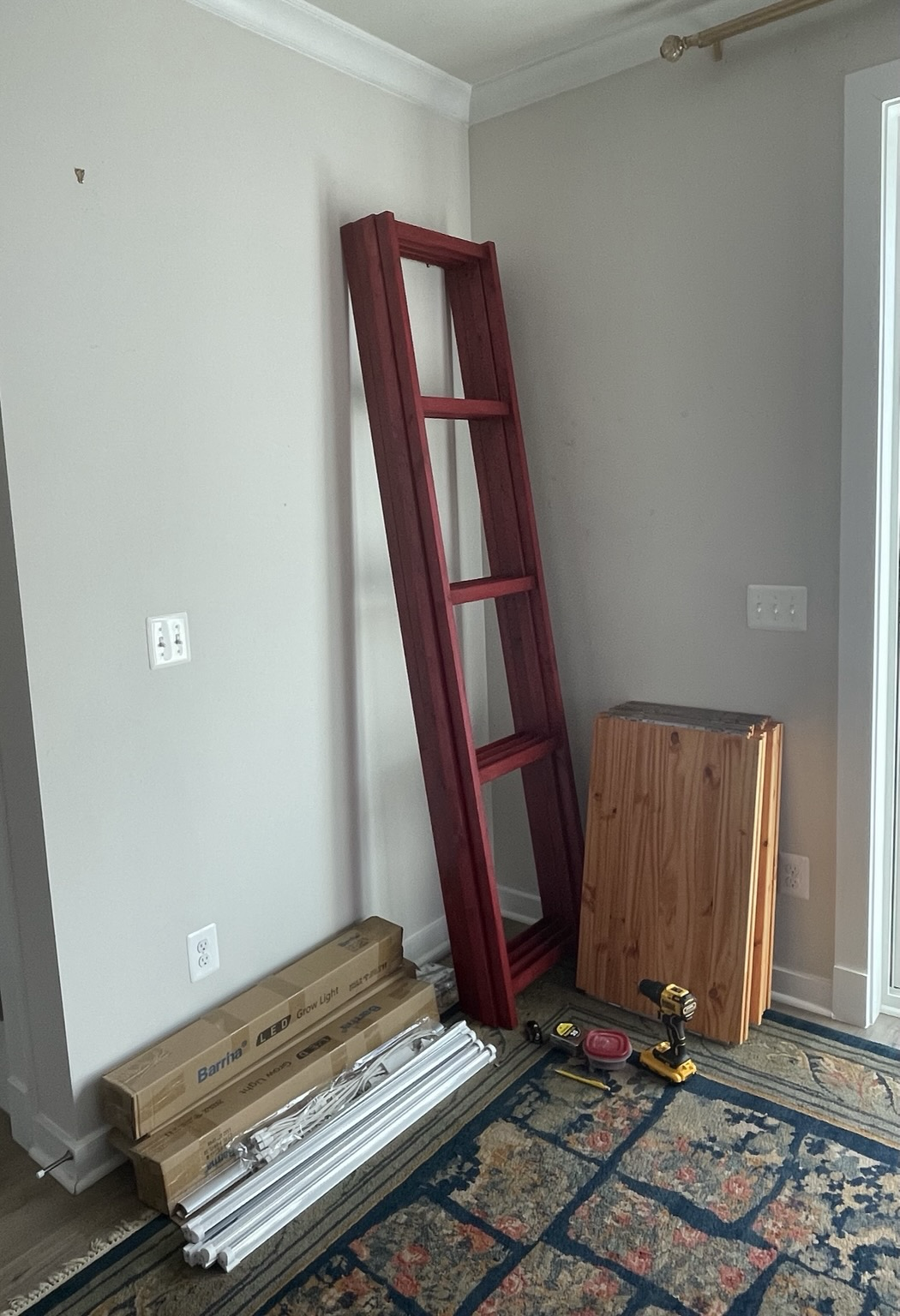 The stained food side rails and shelves are shown stacked against the wall. The side rails are stained a rich full red. The shelves are stained a reddish wooden cherry-wood color. 