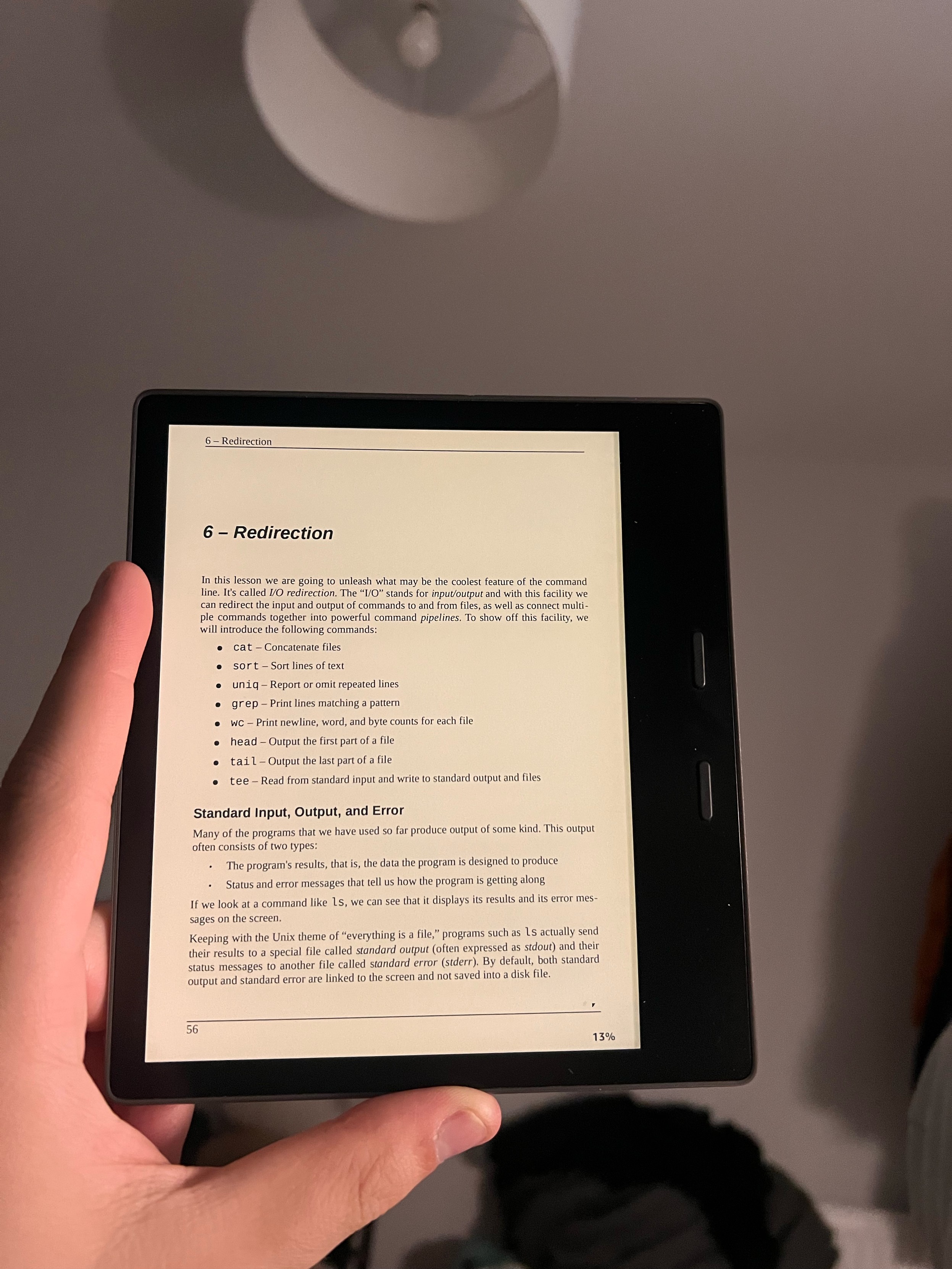 Photo of someone holding a Kindle Oasis with the left hand. We can see that the page being read is titled “6 - Redirection”