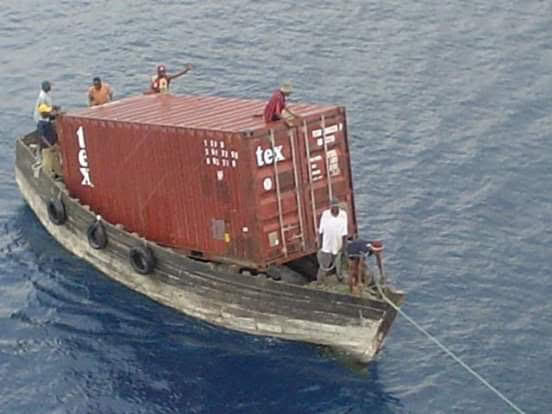 Shipping container loaded on top of a small wooden stern boat which it is clearly too big for