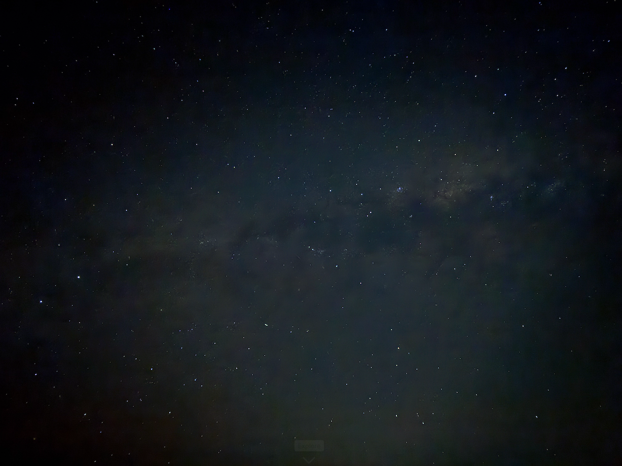 A picture taken with an iphone 15 pro of the night sky in southern Australia, facing south. There are hundreds of stars visible, and the Milky Way can be seen prominently through the bottom third of the picture, a dusty cloud of grey and white and brown, the latter color prominent in the center.