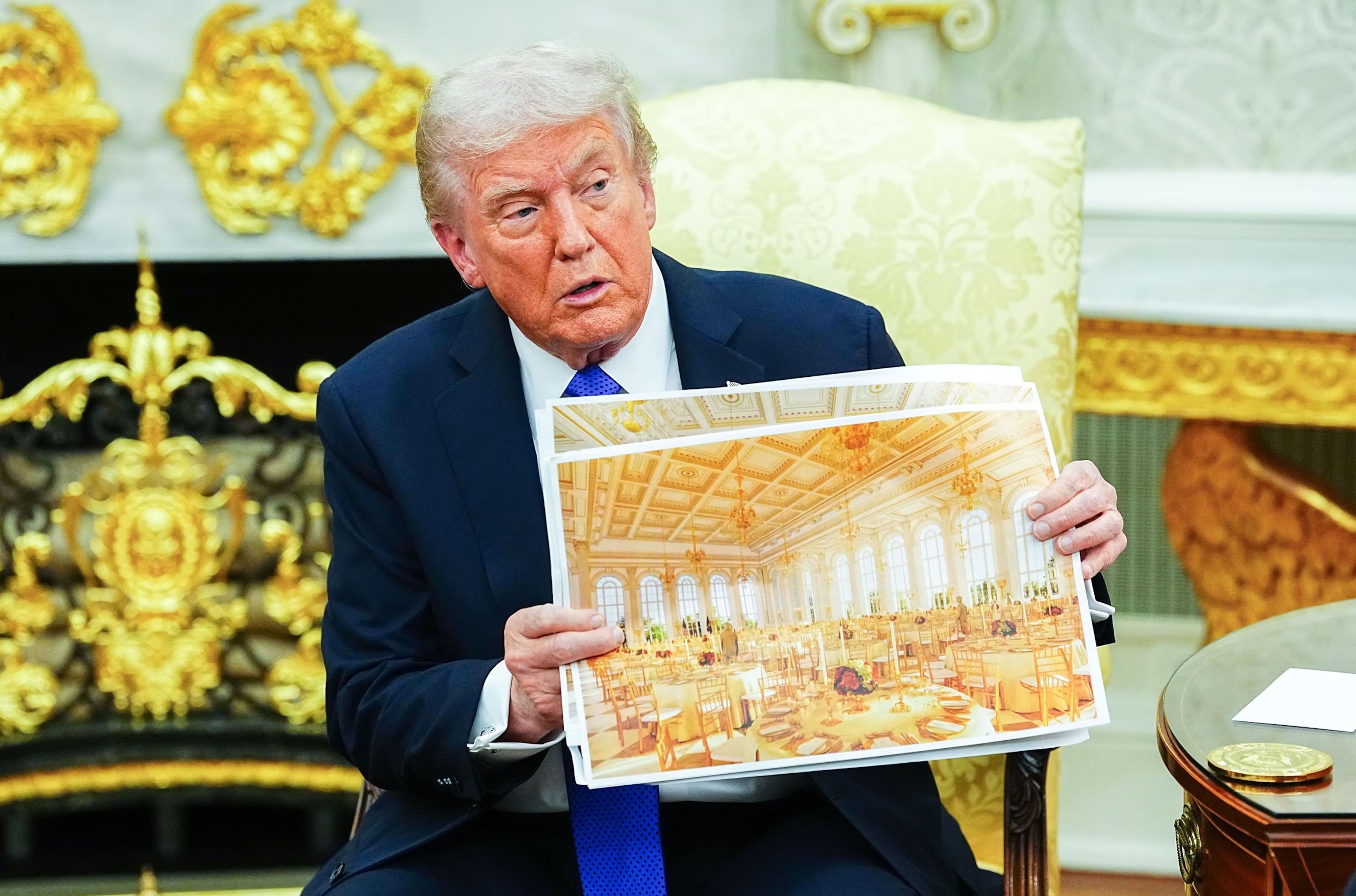 Donald the Terrible in the Oval Office drowning in a sea of gold-plated plastic, brandishes an artist's impression of his fucking goddamned ballroom, in which everything appears to be painted gold.
