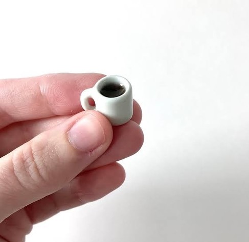 Photo of either a giant person holding a regular sized cup of coffee or a regular sized person holding a very tiny cup of coffee.