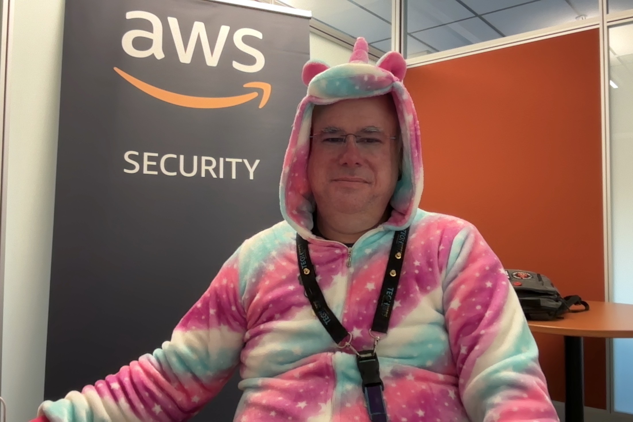 Photo of me sitting in my office, with a pink, white, and blue unicorn onesie.