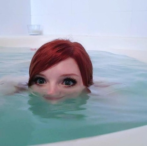 Photo of a pale girl with red hair nose deep in a jacuzzi tub while approaching the edge like excited alligator.