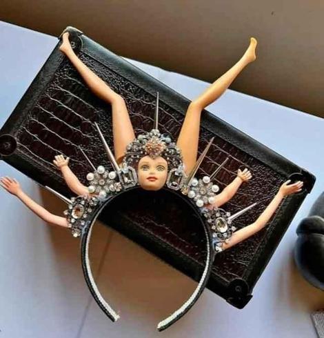 Put of a hair band clip thingy made with costume jewelry, a Barbie head, two legs, and four arms.