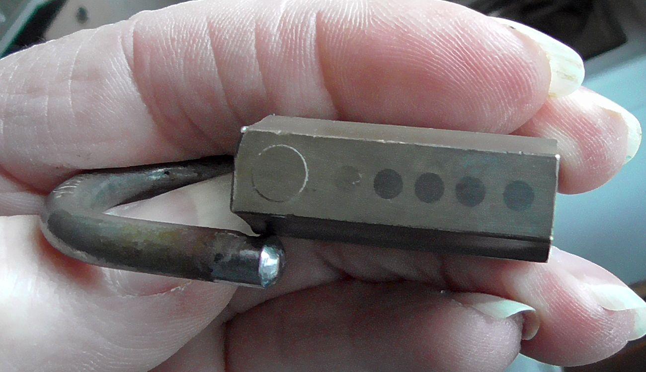 Old brass padlock turned on its side showing brass caps covering top of pin holes and boring for shackle dogs.