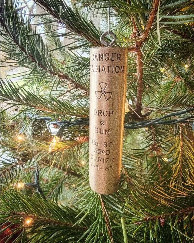 Long cylindrical ornament hanging up on a tree with light with following text written on the front:

DANGER
RADIATION 
☢️ 
DROP 
& 
RUN 

Co 60
3540
Curies
7-1-63