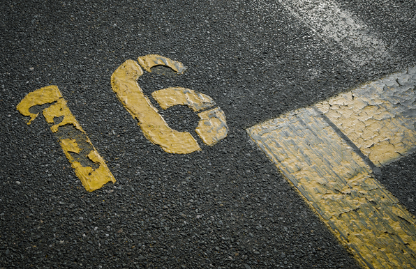 A photo of a blacktop street with yellow lines and the number 16 in stenciled yellow paint.