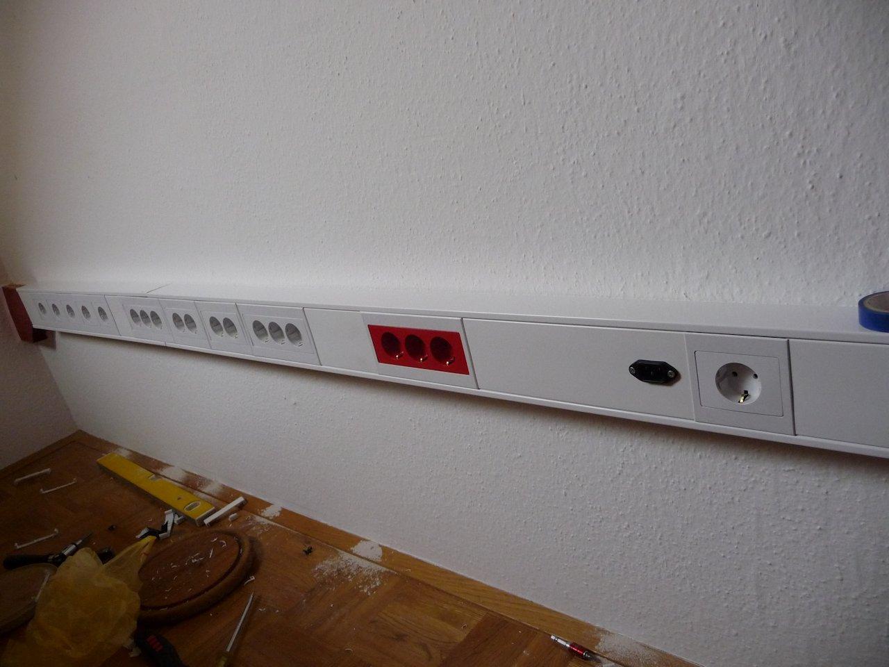 16 white and 4 red Schuko outlets, with different spacings on a wall (the red ones are fed from a black C14 inlet, connected to UPS)