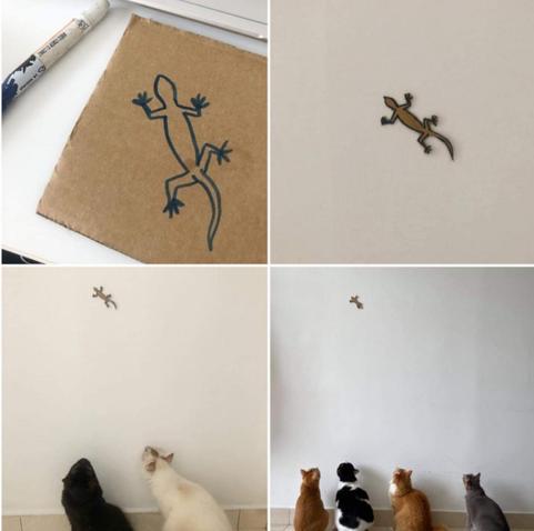 Four panels showing the creation and usage of a cardboard lizard cutout. First panel shows a square piece of cardboard with a lizard drawn on it with a permanent marker. Second shows the lizard cutout and stuck to a wall. Third panel zooms out showing a black cat and white cat staring with great interest from the floor. Last panel shows the lizard (now with a missing tail) even higher on the wall as four different cats stare from below.