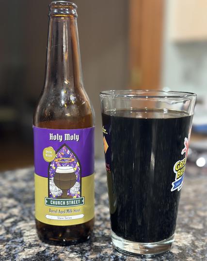 Bottle of Holy Moly stout next to the glass it was poured in. It is a very dark — almost black — drink. 