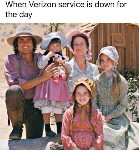The image is a still from the television show "Little House on the Prairie." The image depicts a family of five. On the left, a man wearing a light-brown cowboy hat, a pink and white striped shirt with suspenders, and brown pants is kneeling down. He has a dark complexion and dark hair. He is looking at the camera and smiling. He is holding a young girl dressed in a pink dress, white tights, and black shoes. She is wearing a blue bonnet and holding a doll. The girl is also smiling at the camera…