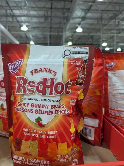 The image is a close-up shot of a bag of "Frank's RedHot Spicy Gummy Bears." The bag is the central focus, positioned slightly off-center.

The bag is predominantly red, with a gradient effect that transitions from a deeper red at the top to a lighter, orange-red towards the bottom. The brand name "Frank's RedHot" is prominently displayed in large, bold, white letters with a red outline. Beneath this, "ORIGINAL / ORIGINALE" is written in smaller text. The product description "SPICY GUMMY BEARS …