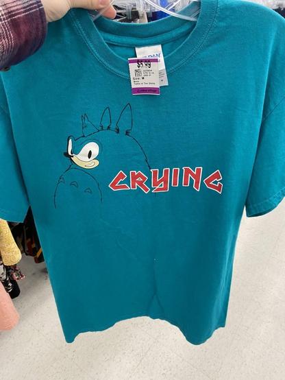 Blue / blue-teal knockoff brand shirt with a combo Sonic the Hedgehog and Totoro figure that has a Sonic face. Written on the shirt is the word 'CRYING' in red letters. It's good to show others what your hobbies are 😭