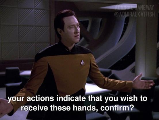 The image is a meme featuring a still from the Star Trek: The Next Generation television series. The primary subject is the character Lieutenant Commander Data, portrayed by Brent Spiner, who is an android. He is wearing a Starfleet uniform, which consists of a dark navy or black undershirt with a prominent gold or tan yoke and sleeves. A small Starfleet delta insignia is visible on the left side of his chest. Data is looking slightly off-camera to his left, with a thoughtful or inquisitive exp…