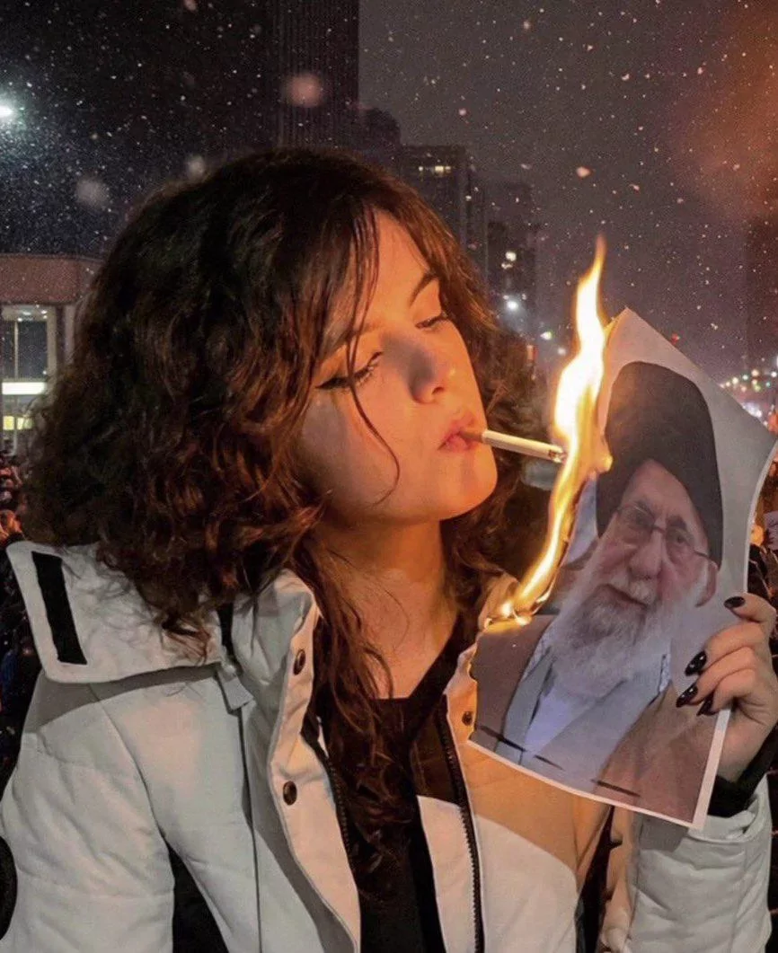 A young Iranian woman lighting her cigarette with a burning picture of (former) Ayatollah Khamenei