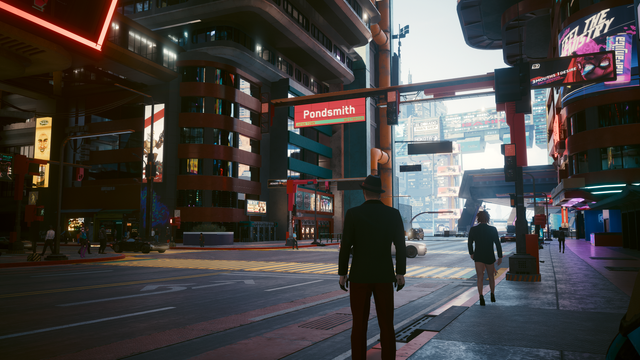Screencap from Cyberpunk 2077

In the foreground, we see the back of a person wearing a fedora hat, a dark suit jacket, and dark trousers with a reddish hue. They are standing on a sidewalk or pedestrian area, facing away from the viewer and towards the street. To the right of this individual, another person is walking away from the camera, also viewed from behind, wearing a dark jacket and black shorts, with high heels. Their presence suggests this is a location with pedestrian traffic.

The s…