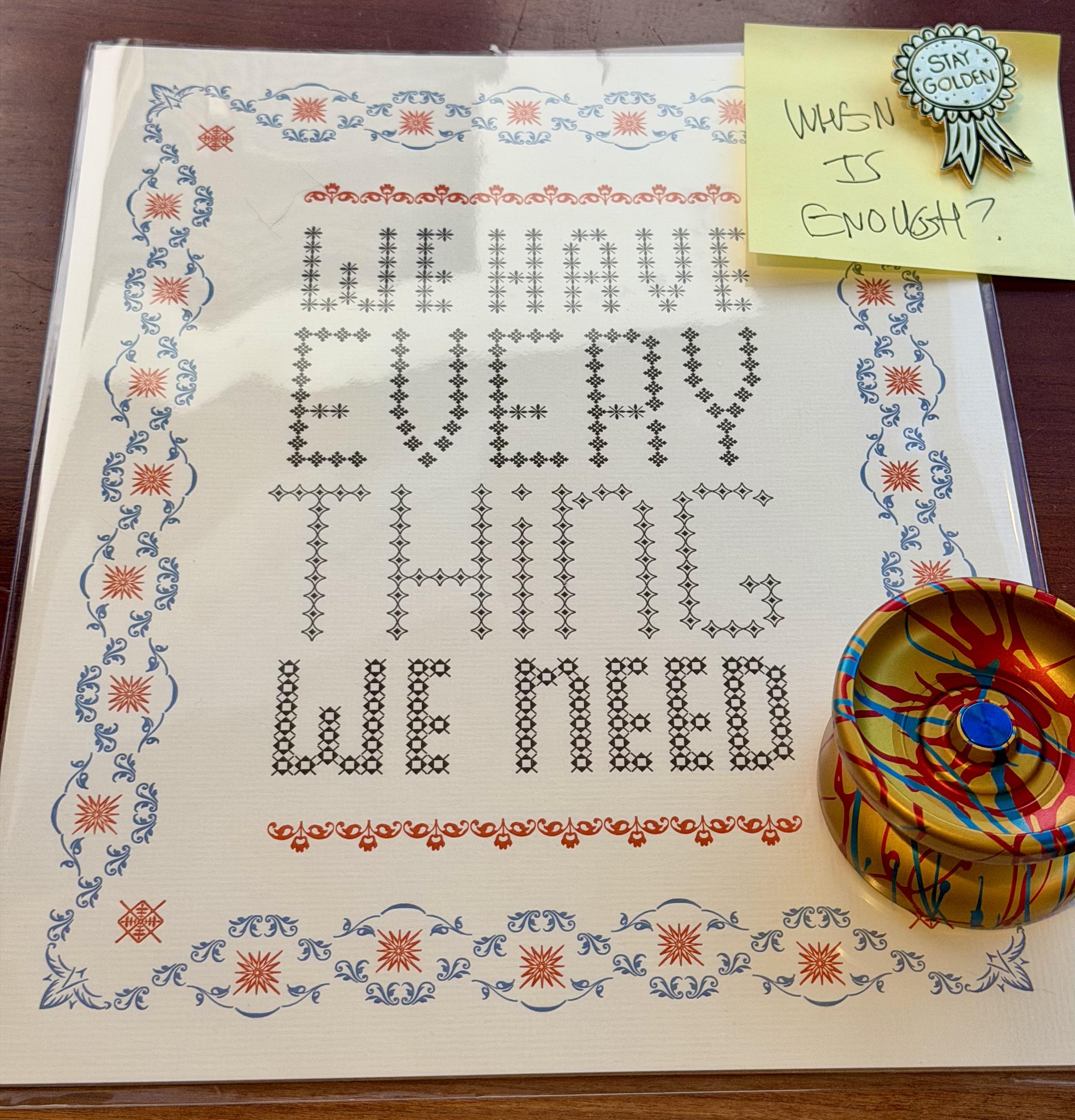Linotype print of “we have everything we need” with a yo-yo and a stay golden pin, and a post it note that has “when is enough?” written on it