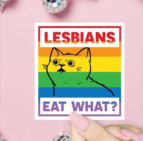 Photo of someone with long pink nails holding a rainbow colored pride sticker with a nervous cat saying, "Lesbians eat what?"