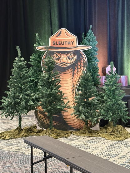 A snake in the forest wearing a ranger hat that says Sleuthy.