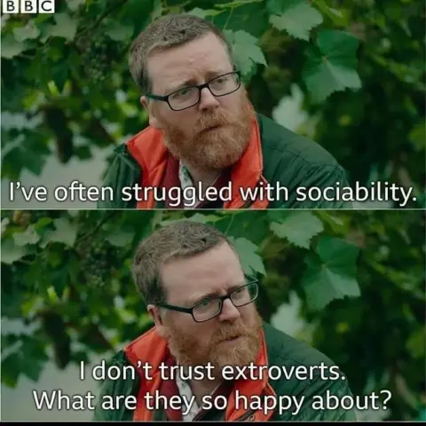 The image is a meme featuring two horizontal panels, each depicting a close-up of Frankie Boyle, a middle-aged man with reddish-brown hair and beard, wearing glasses and an orange vest over a green jacket. Both panels have white text superimposed on them.

In the top panel, the man is looking slightly off-camera to his left with a contemplative expression. The text reads: "I've often struggled with sociability." The background is blurred green foliage, with hints of grape clusters. A small BBC …