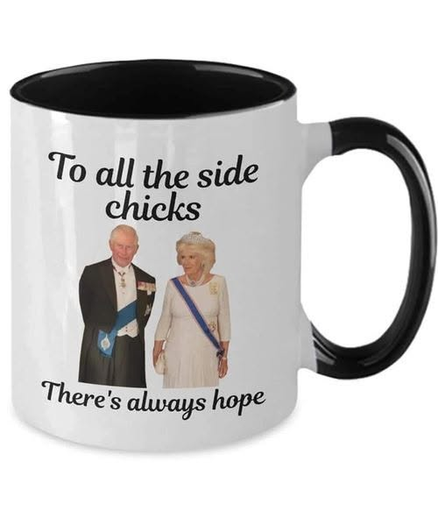 The image shows a white ceramic mug with a black interior and handle. The mug has text and an image printed on its exterior. The text at the top of the mug reads, "To all the side chicks" in a stylized black font. Below the text, there is an image of a man and a woman, presumably King Charles III and Queen Camilla, standing side-by-side. The man is on the left, wearing a formal black suit with a blue sash and medals. The woman is on the right, wearing a light-colored dress and a tiara, with a b…