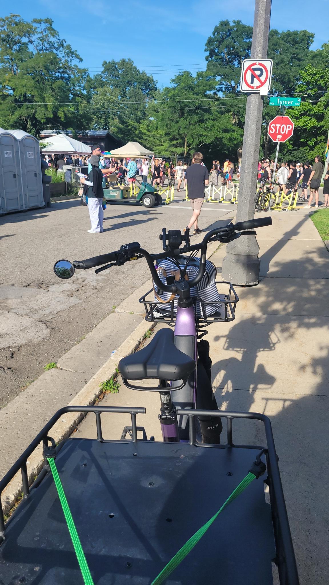 Bike parked on sidewalk in front of a group of people at a pride event.
