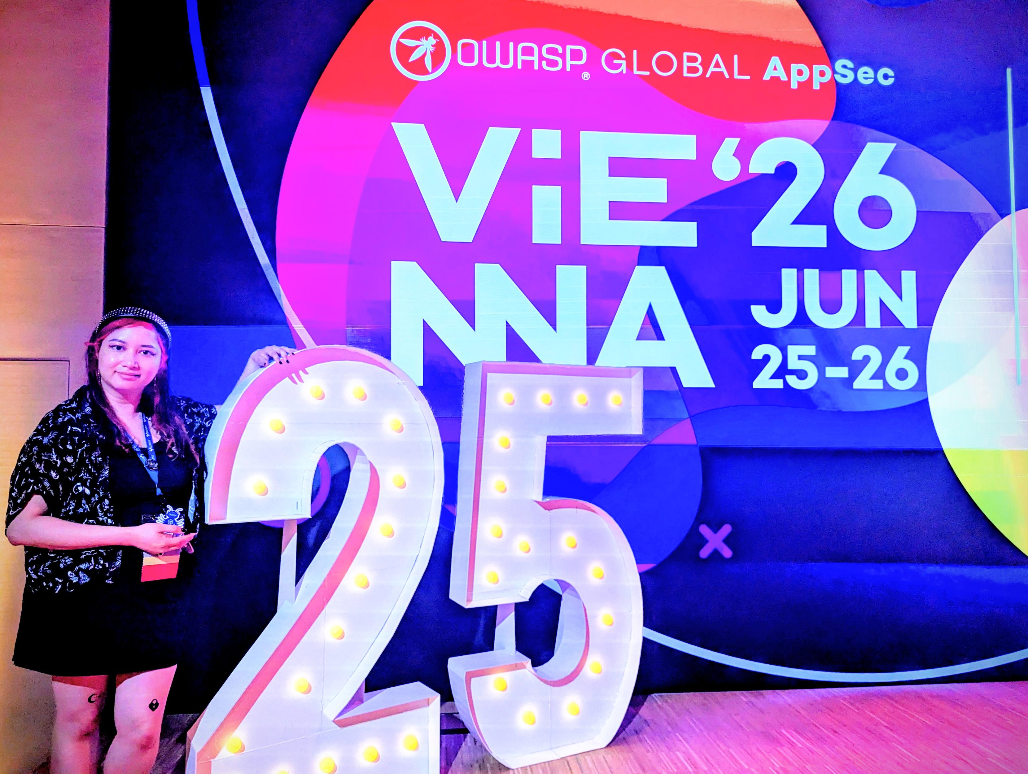 Maria is next to a big 25 standee and in front of the OWASP Global AppSec Vienna '26 June 25-26 sign on the big screen