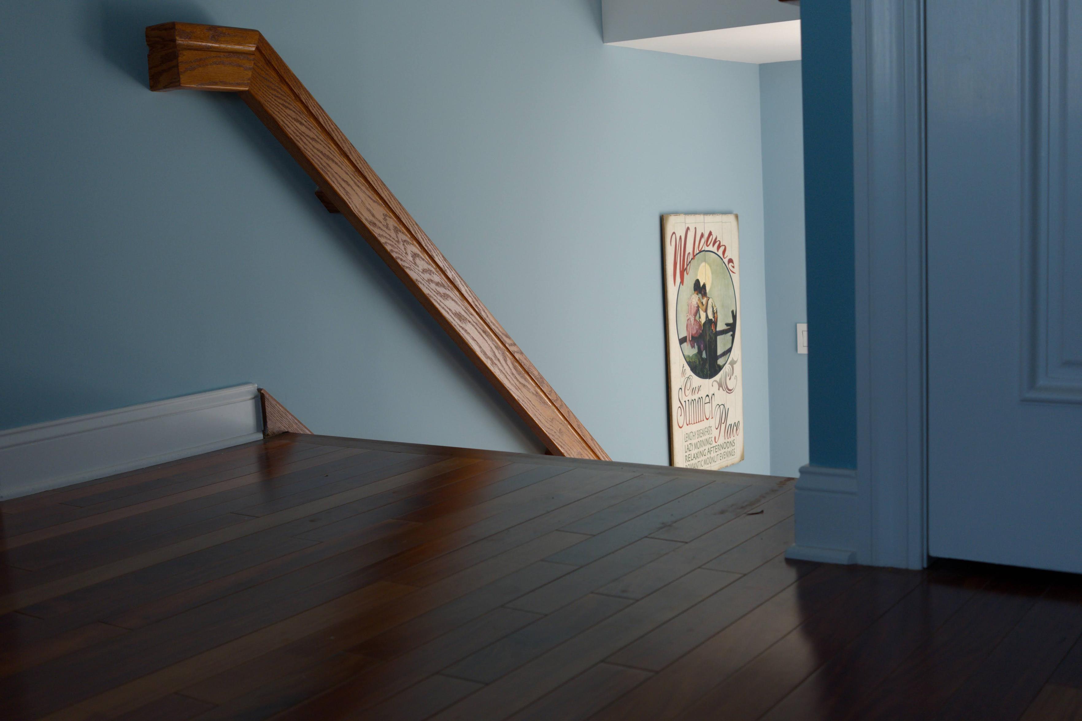 The view from a foot or so off the ground in a home painted blue. Hardwood floors run down towards the stairs. The railing is a leading line into the source of sunlight from below.