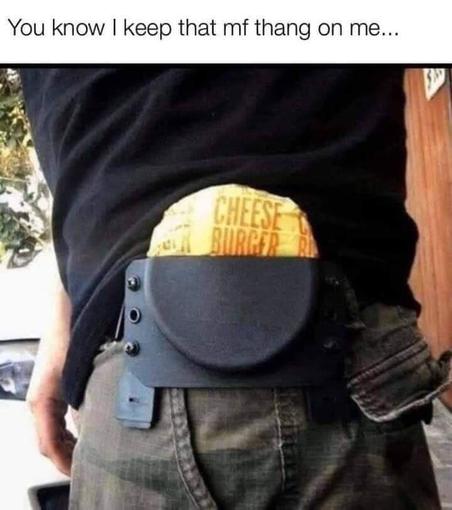 The image is a close-up, waist-level shot of a person wearing a black t-shirt and camouflage-patterned pants. Attached to the person's belt is a black holster, commonly used for carrying a firearm. However, instead of a weapon, a yellow wrapper with the words "CHEESE BURGER" printed in large, bold, orange letters is sticking out of the holster. The wrapper appears to be from a fast-food item, likely a cheeseburger. The person's hand is visible on the left side of the frame, resting near the hol…