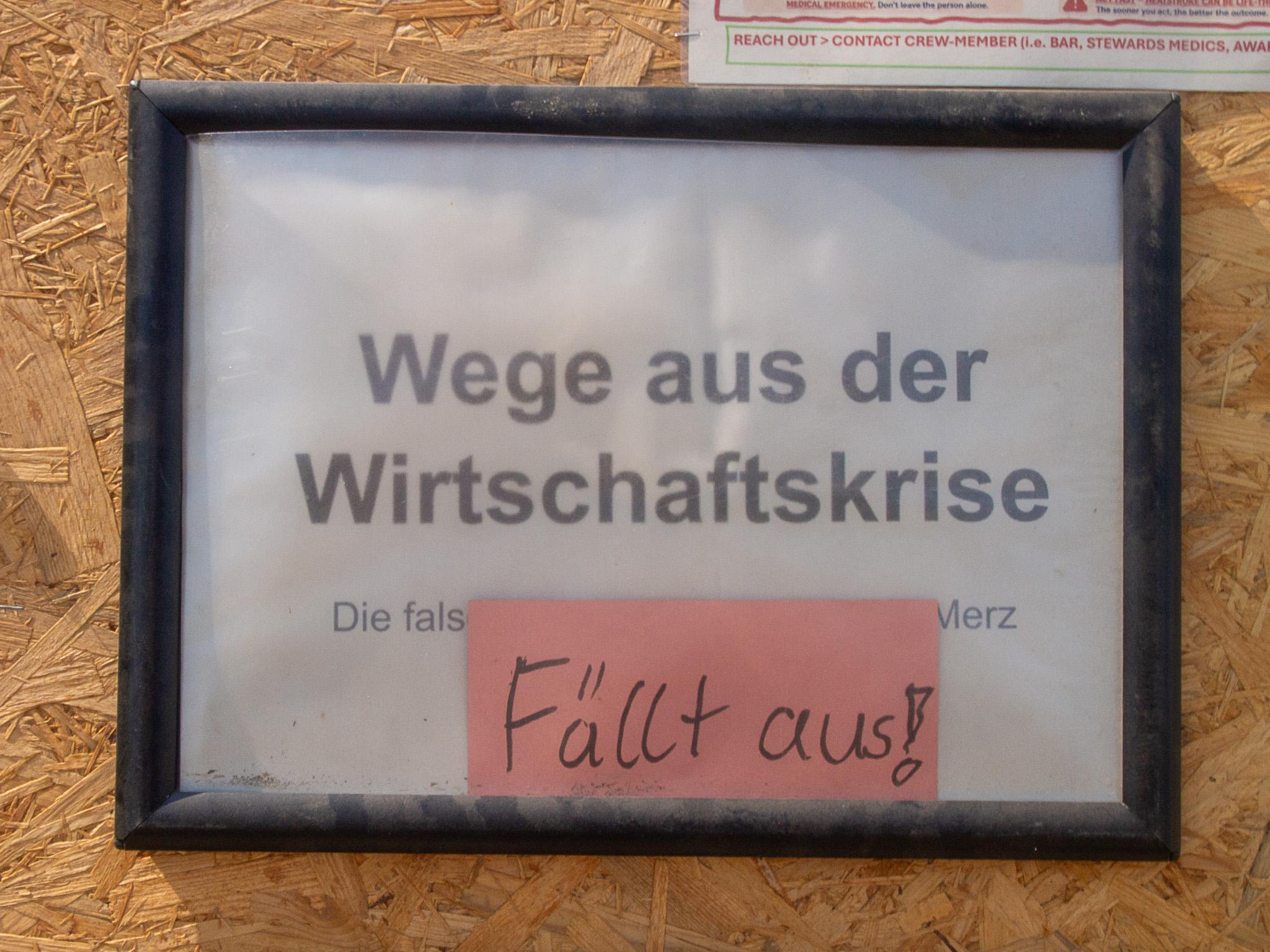 Gerahmte Veranstaltungsankündigung "Wege aus der Wirtschaftskrise" mit handgeschriebenem Zettel "Fällt aus!"
