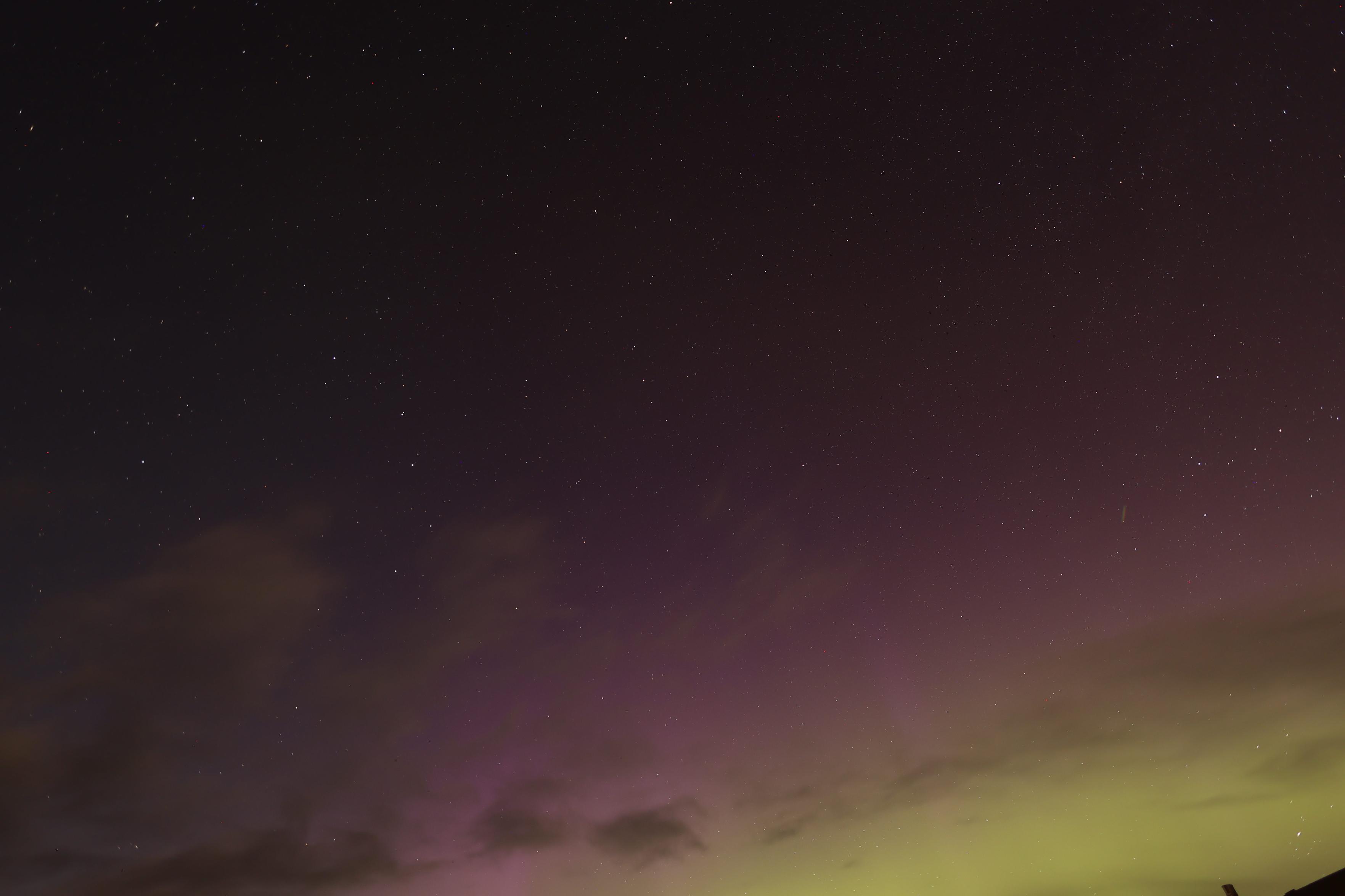 A night sky that is a mix of yellow, purple, clouds and a few stars