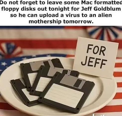 The image features a humorous meme overlaid on a photograph. The text at the top of the image reads "Do not forget to leave some Mac formatted floppy disks out tonight for Jeff Goldblum so he can upload a virus to an alien mothership tomorrow."

The photograph itself shows a white plate filled with several black 3.5-inch floppy disks. These disks appear to be vintage technology. To the right of the floppy disks, a small white card is propped up, displaying the handwritten text "FOR JEFF" in bla…