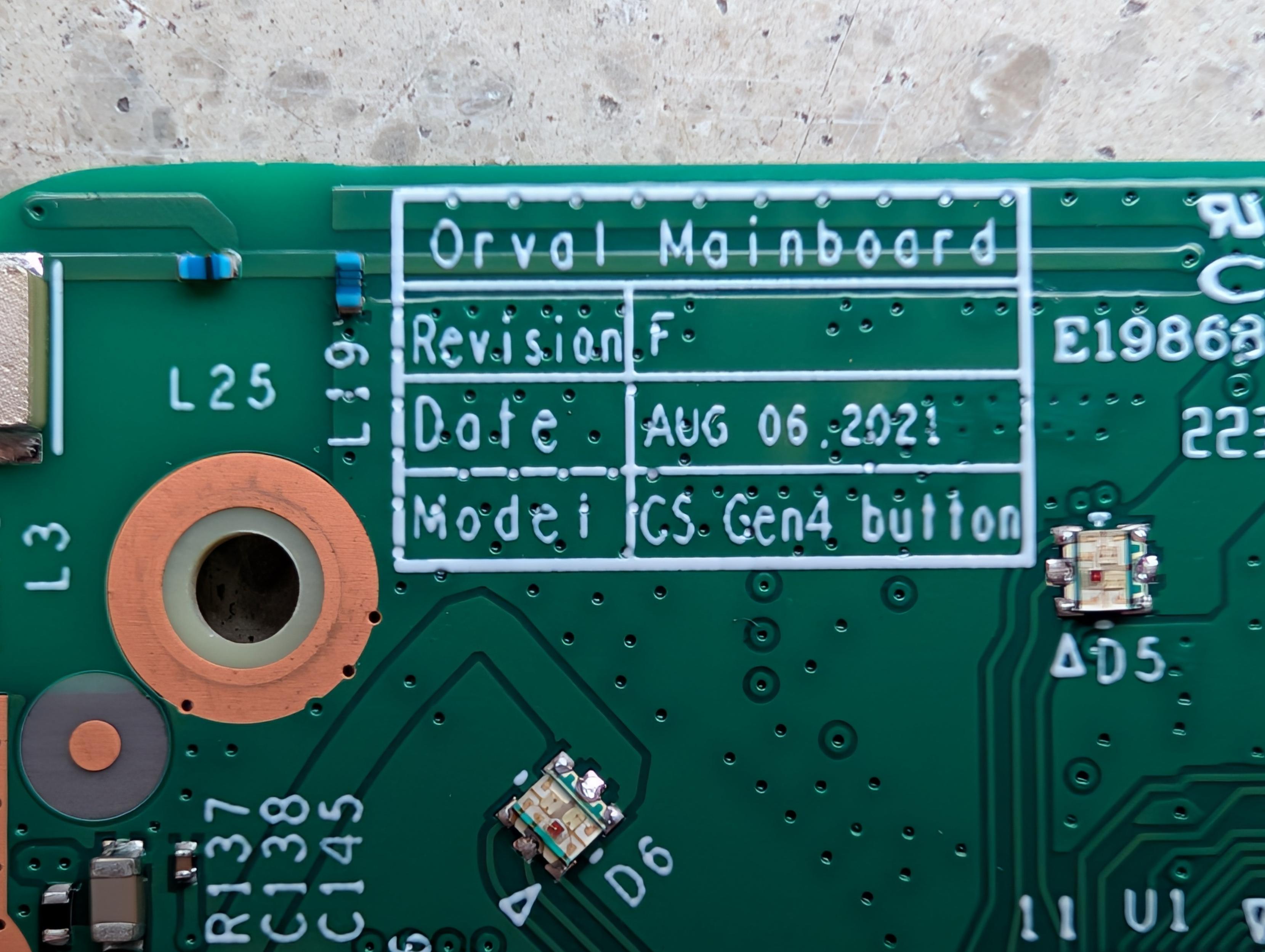 Close-up shot of a green printed circuit board (PCB) with white silk-screened text inside a rectangular box reading "Orval Mainboard", "Revision F", "Date AUG 06, 2021", and "Model CS Gen4 button". Electronic components like resistors, capacitors, and tiny LED indicators are visible around the text.