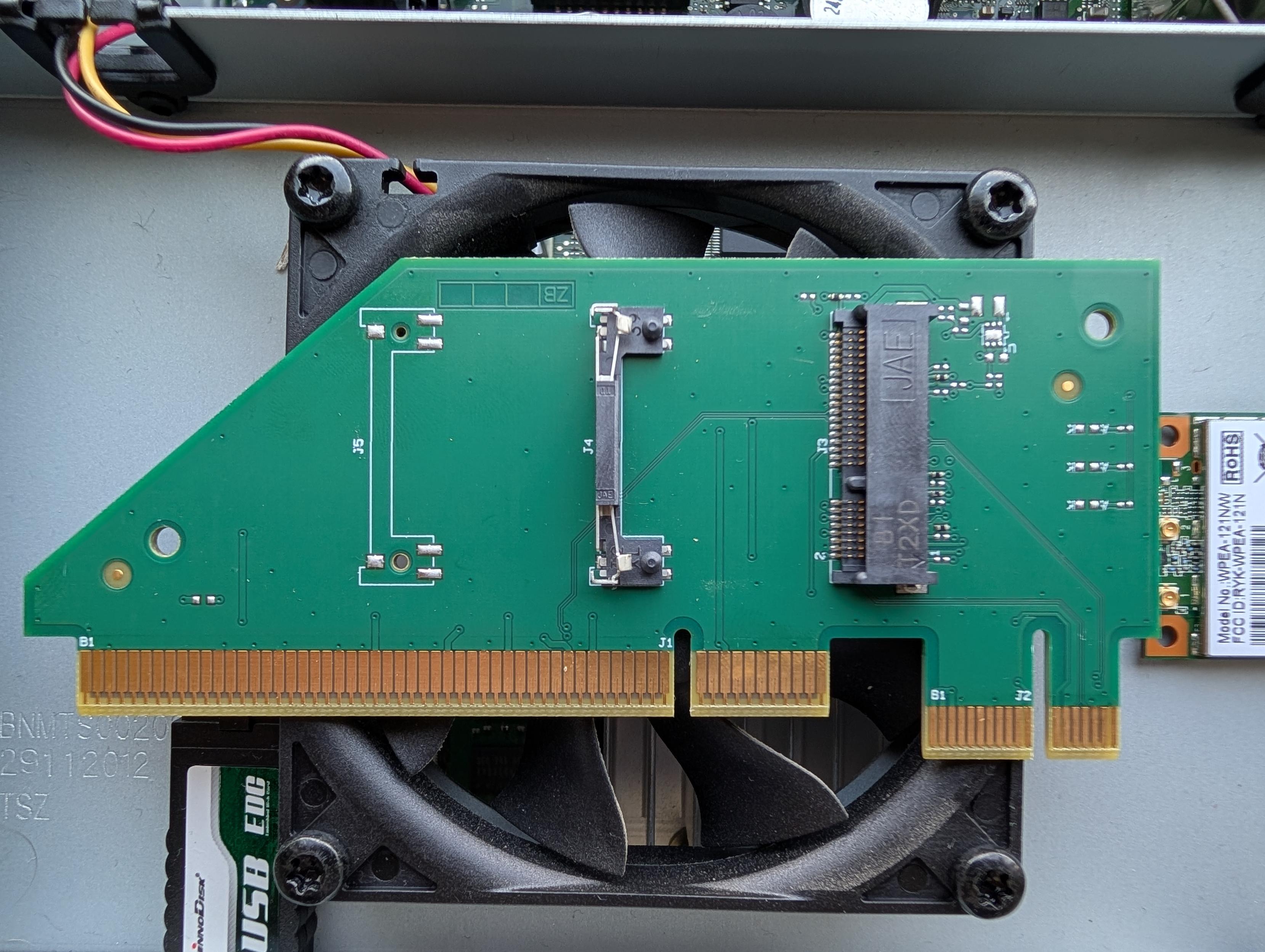 A green riser card with golden edge contacts rests on a black case fan.