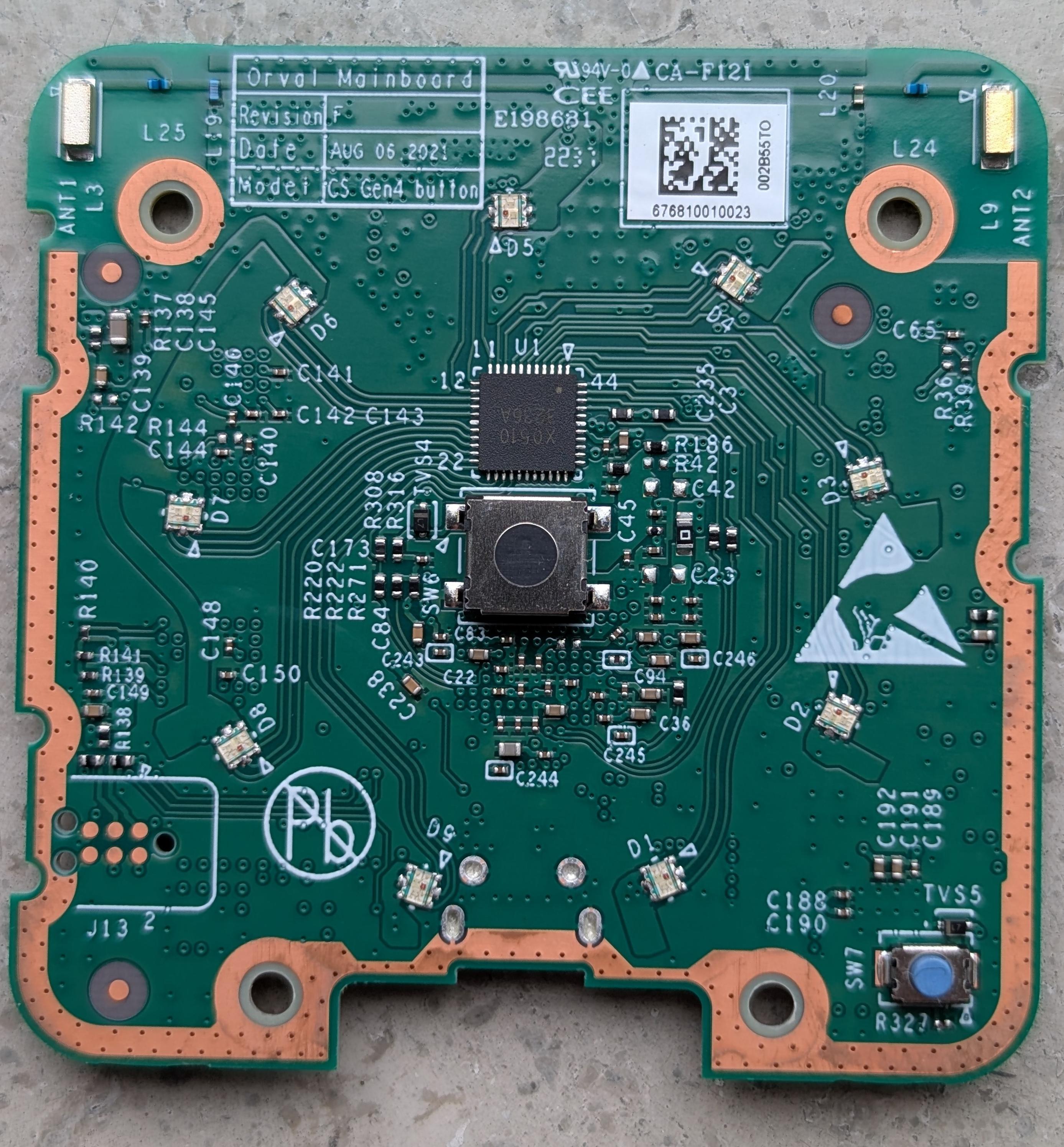Green printed circuit board labeled "Orval Mainboard Revision F" featuring various surface-mount components, resistors, and capacitors. A square integrated circuit chip and a tactile button switch are mounted in the center, flanked by gold antennae at the top corners.