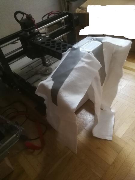 A 3018 CNC machine extended with an arm(?) pushing/turning the spindle downwards, thereby removing z-axis slack. Three pieces of molton fabric have been attached to the arm with tape.