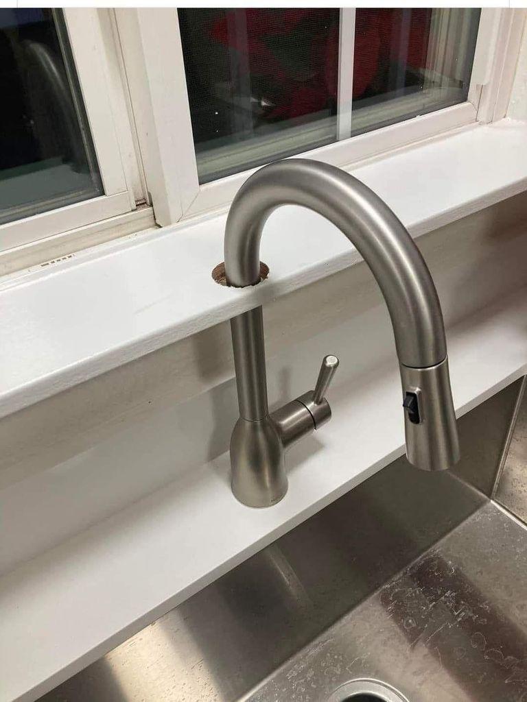 A kitchen faucet that extends up from the countertop through a hole in the window sill above and then finally arcs over to point down toward the sink.
