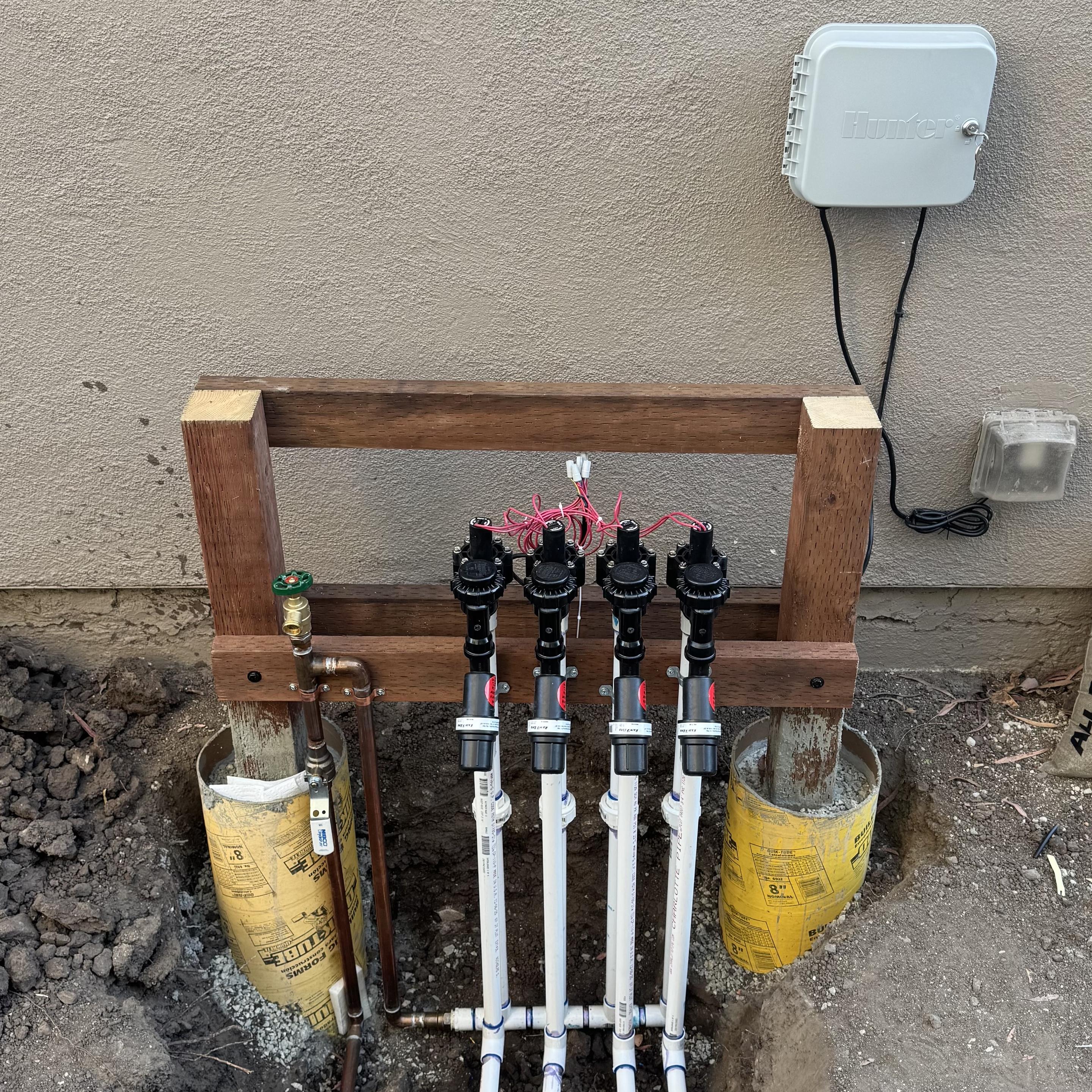 Photo of a copper supply line feeding a hose bibb and a manifold on which four irrigation valves and filters feed a set of landscaping lines.