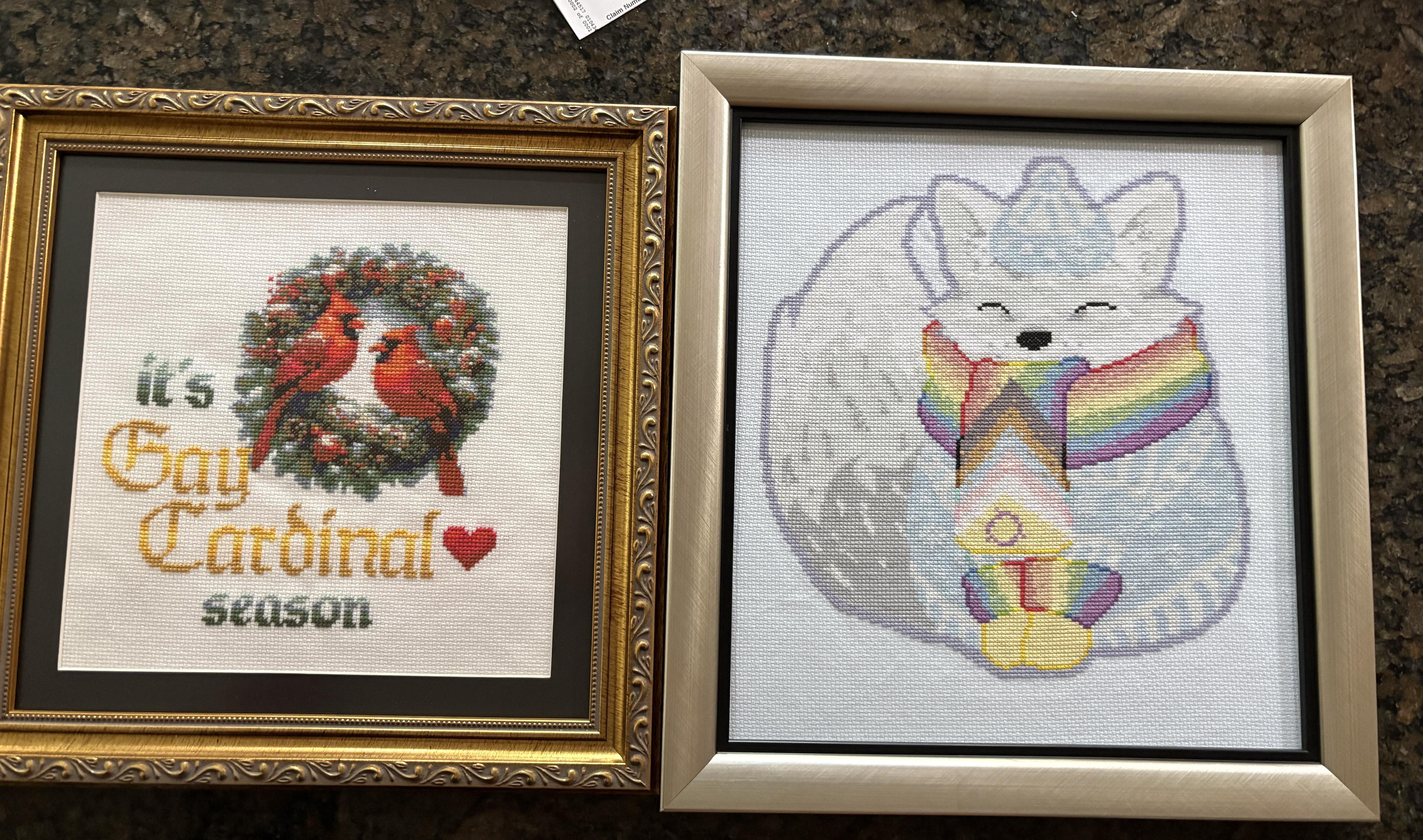 Two cross stitch pieces. One is an arctic fox wearing a pride scarf. The other shows two red cardinals on a wreath and reads “it’s gay cardinal season”