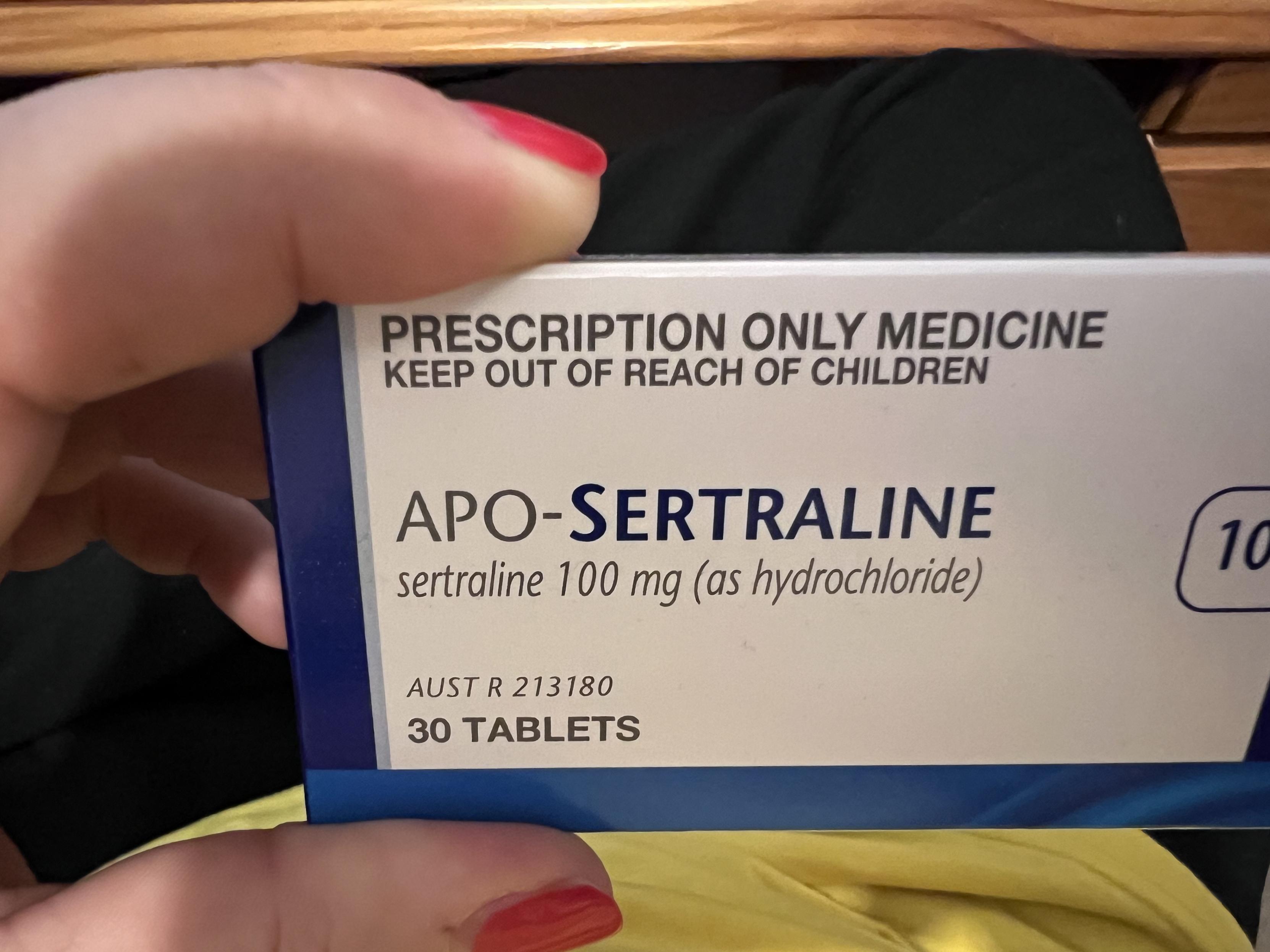 A hand with red painted nails holding a box of 100mg Sertraline tablets