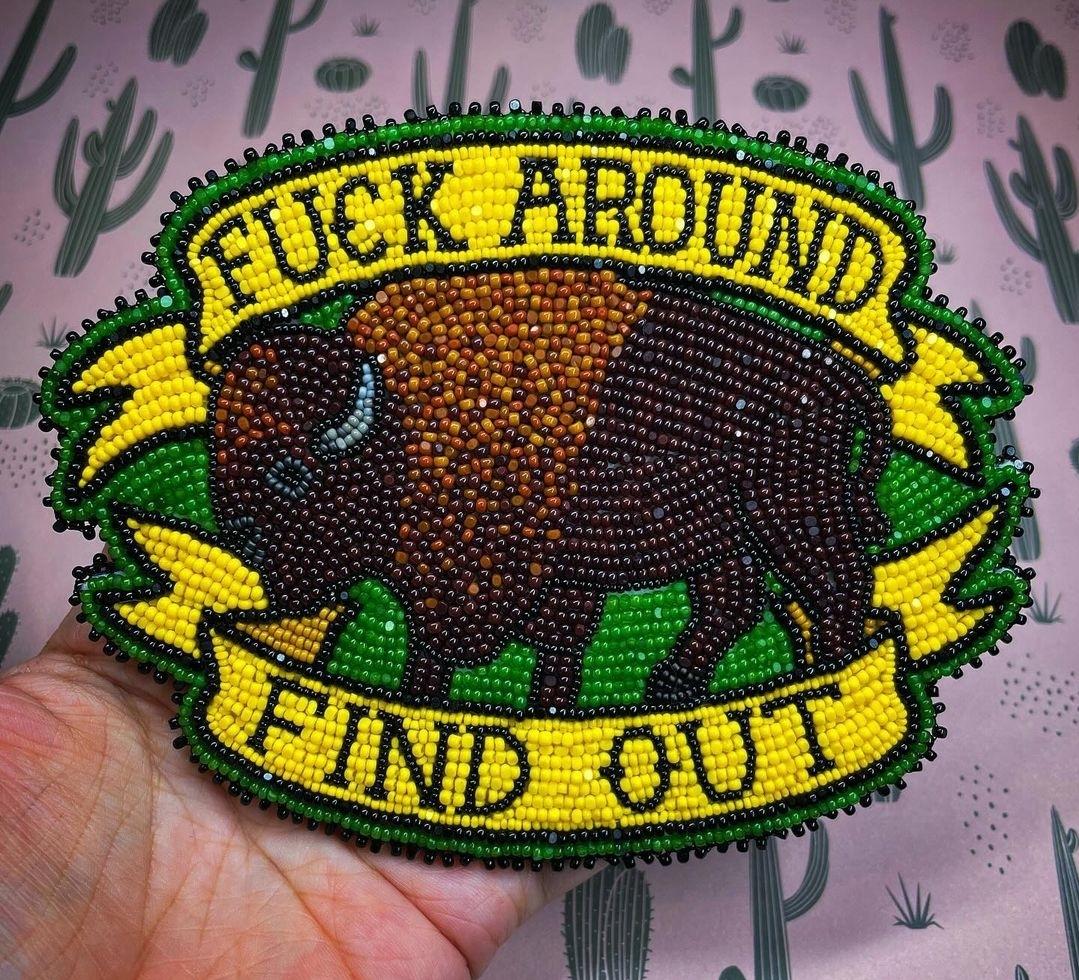 Beadwork of a turtle island bison with yellow banners above and below stating fuck around, find out.