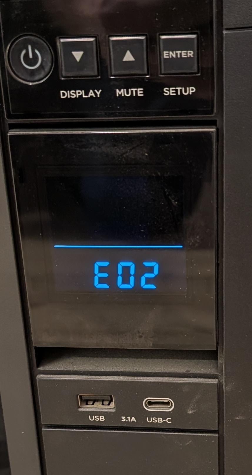 Display screen on the front of an Uninterruptible Power Supply (UPS). In lighted blue letters and numbers the display shows “E02.” Above the display are four buttons, left to right: On/Off, Display, Mute, and Setup.